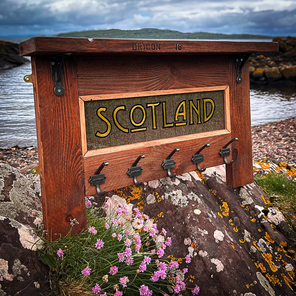 A wooden coat rack with harris tweed inlay and gilded 'Scotland' typography.