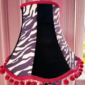 A zebra print and black lampshade with a pink pom pom trim